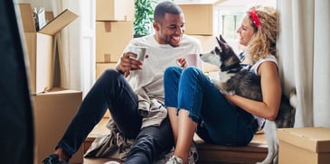 A young couple moving into their first home, drinking coffee and smiling with their dog