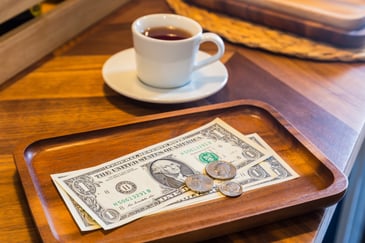 A cash tip sits on a cafe tray beside a cup of coffee