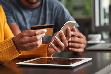 hands holding a credit card and a smartphone over a tablet