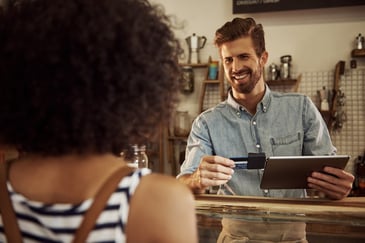A woman pays a barista using a credit card swiped on a tablet