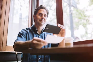 A man uses his smartphone to deposit his check while at a cafe