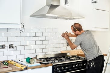 Man tiling a kitchen backsplash during a home renovation project.
