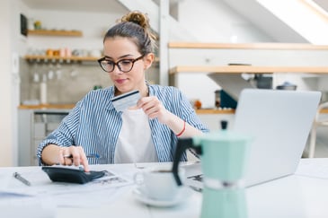 A woman with glasses using a credit card and a calculator