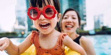 A young daughter in a float with sunglasses on, being held by her mother