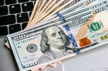 Close-up of a stack of $100 bills spread out over a laptop keyboard.