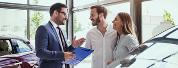 A couple speaks with a salesperson about buying a new car on the floor of a dealership