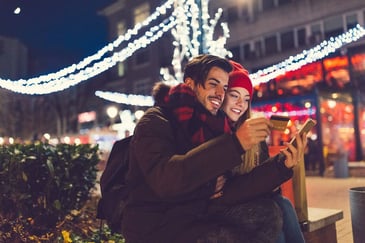 A couple looking at a rewards card while outside under holiday lights