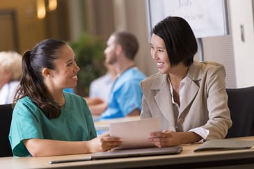a woman wearing nursing scrubs speaks with a financial advisor
